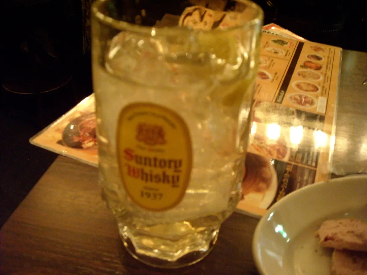 A frosted mug of whisky highball with ice and lemon on a dim bar table, a menu behind it