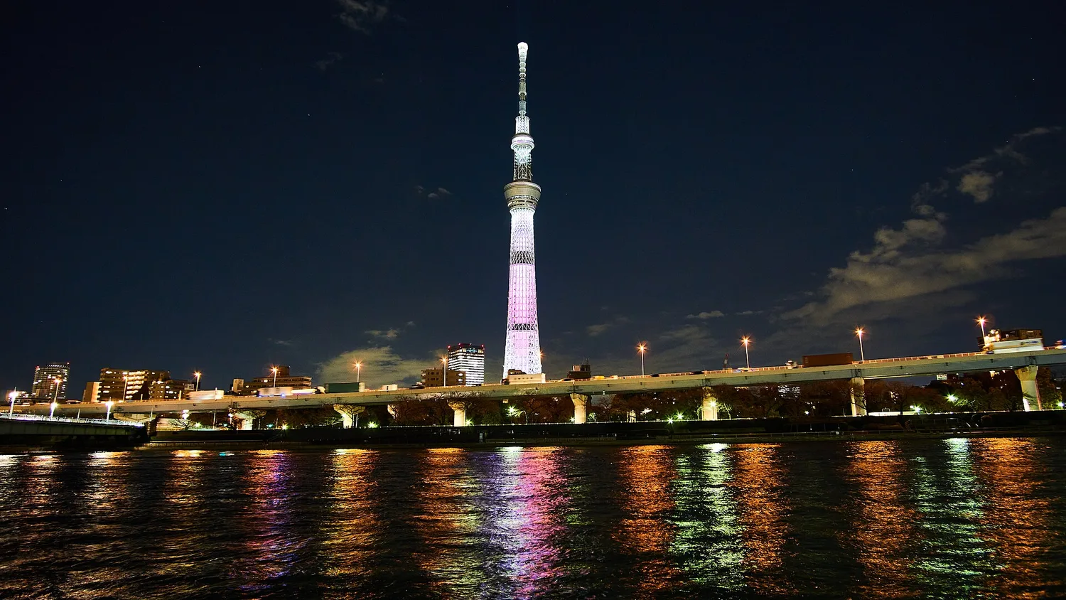 Tokyo Skytree lit in pink at night, with colorful reflections of light on the Sumida River