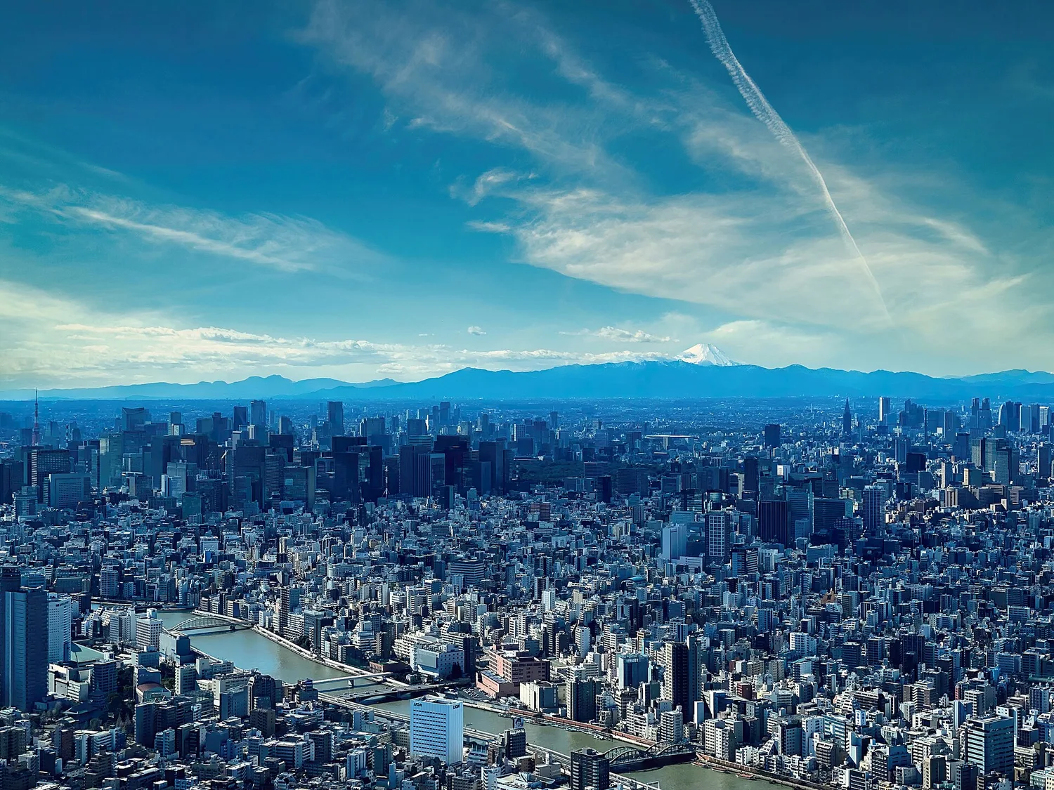 View west from Tokyo Skytree over the Sumida River and the dense city, with Mt. Fuji faint on the horizon