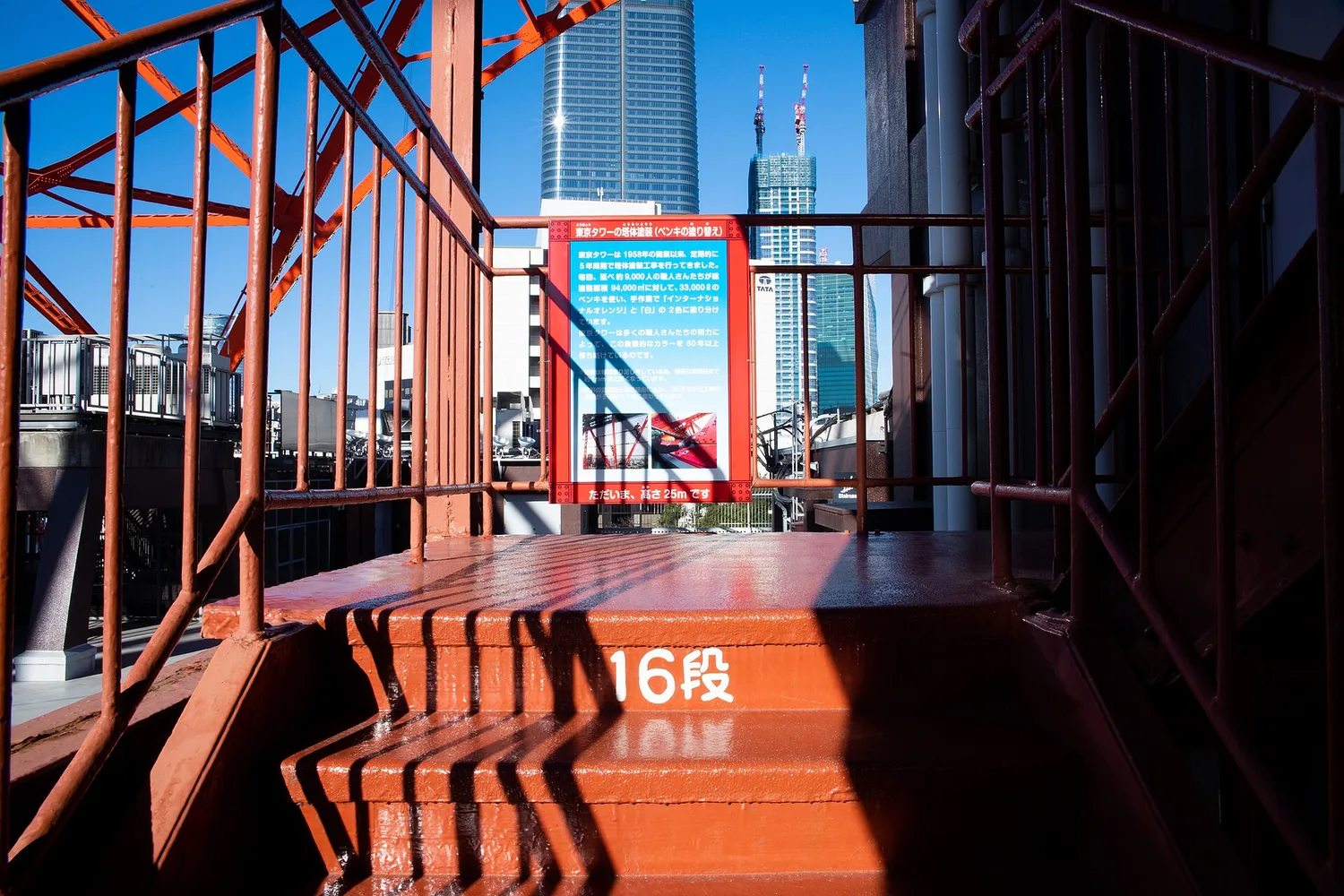 A red landing on Tokyo Tower's open-air stairs with a step-number sign and city buildings beyond the railings