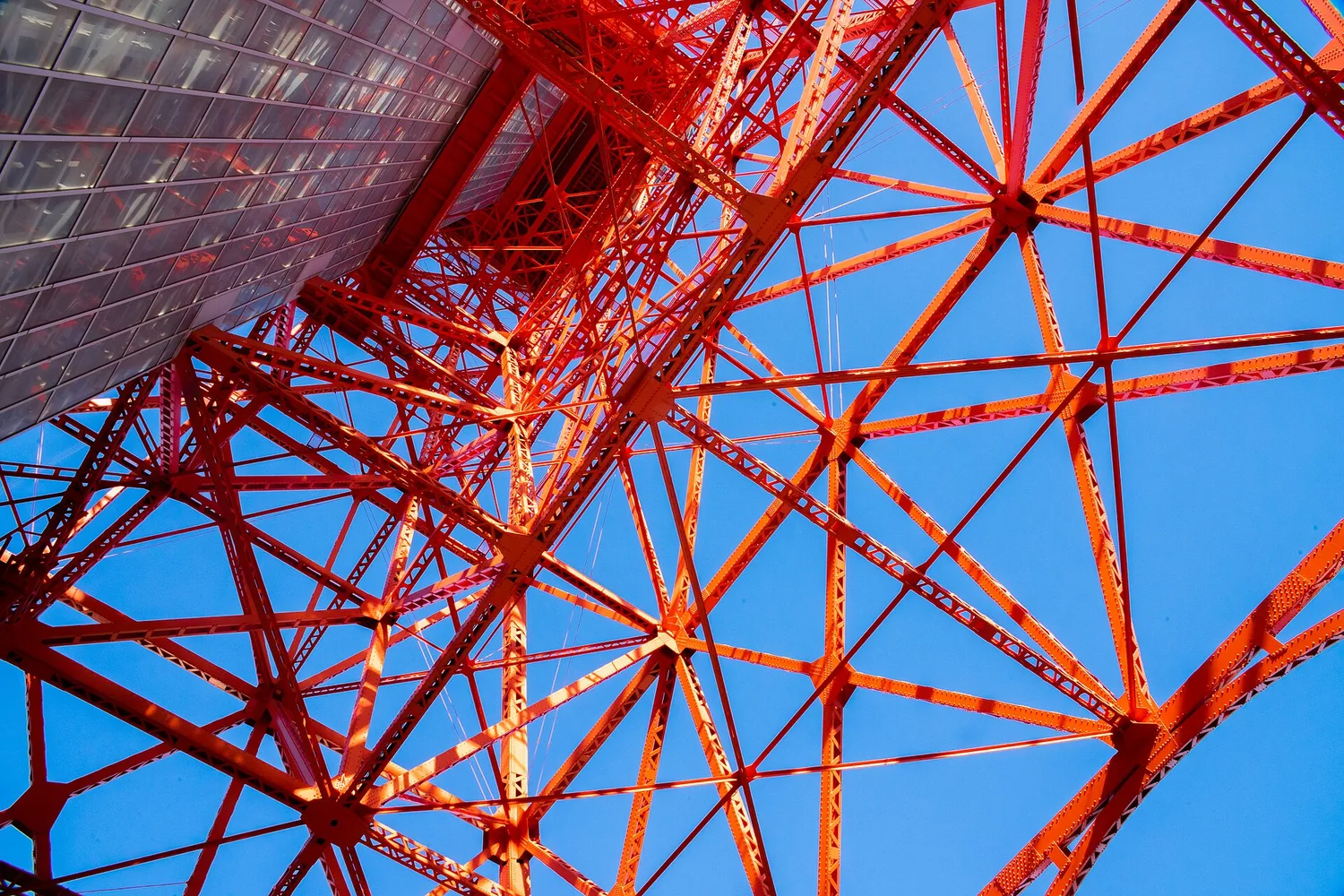 Looking up into the orange and white steel lattice of Tokyo Tower against a deep blue sky