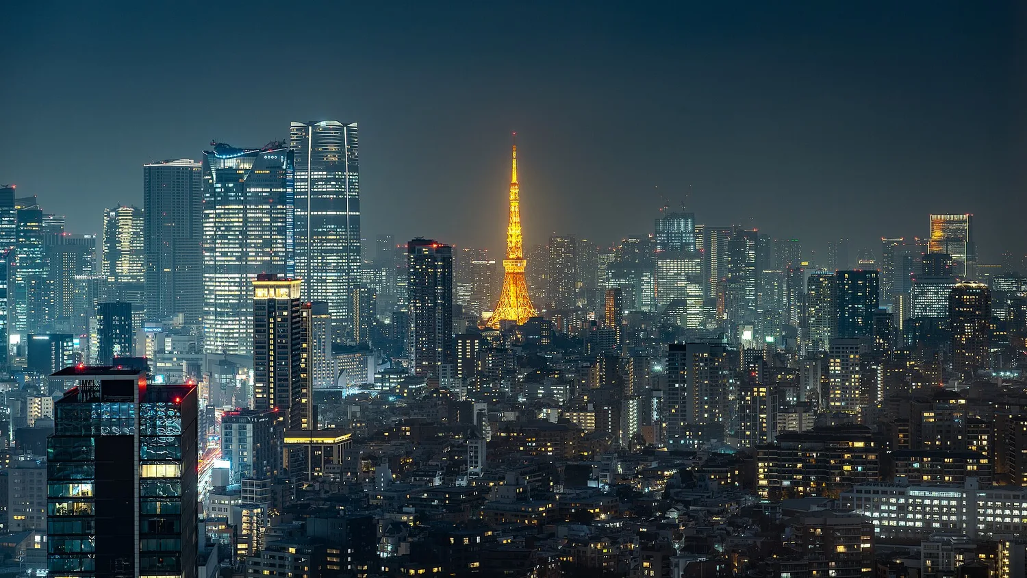 Tokyo Tower glowing in its orange Landmark Light among the night towers of Minato City