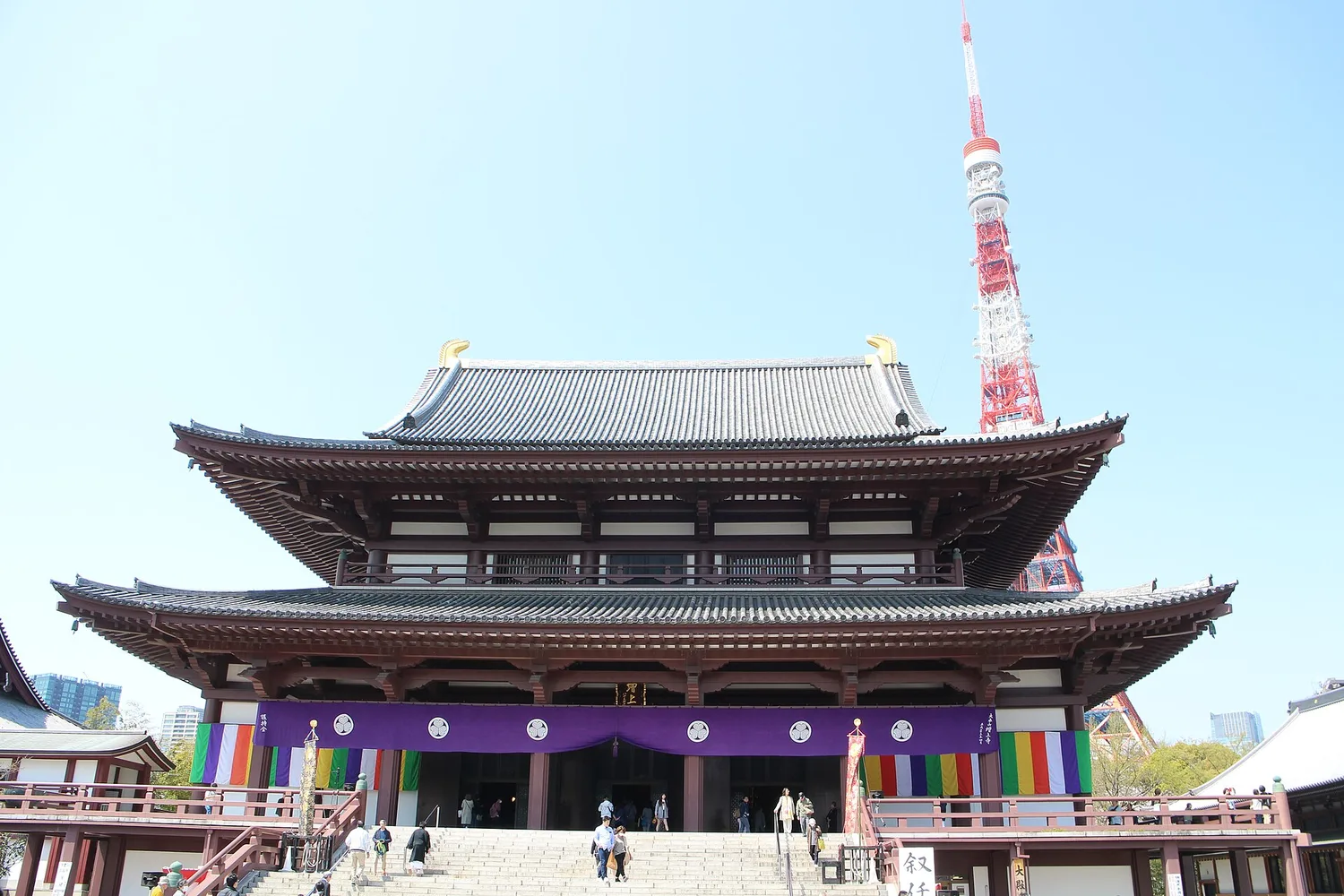 The main hall of Zojoji temple with Tokyo Tower rising behind its roof under a blue sky