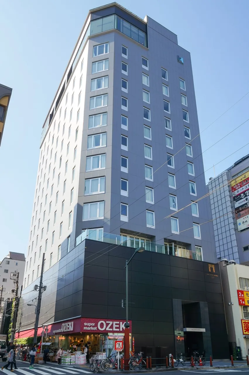The slim grey fourteen-storey building of The Gate Hotel Kaminarimon on an Asakusa street, its top floors glazed, with overhead wires in front