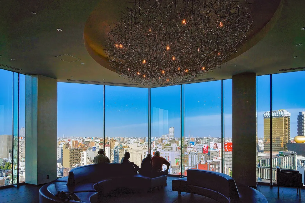 The 13th-floor lobby lounge of The Gate Hotel Kaminarimon, with a glowing ceiling and floor-to-ceiling corner windows looking over the rooftops of Asakusa