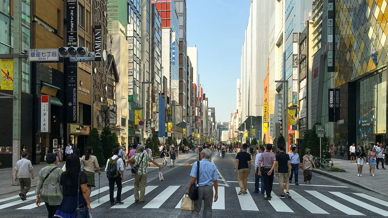 Chuo-dori in Ginza on a Saturday afternoon, closed to cars, with people walking across the wide street between department stores