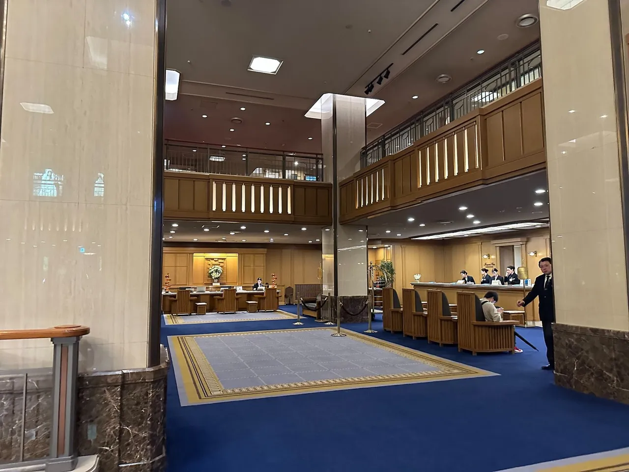 The main lobby of the Imperial Hotel, Tokyo, with a blue carpet, armchairs and a wooden gallery around the high space