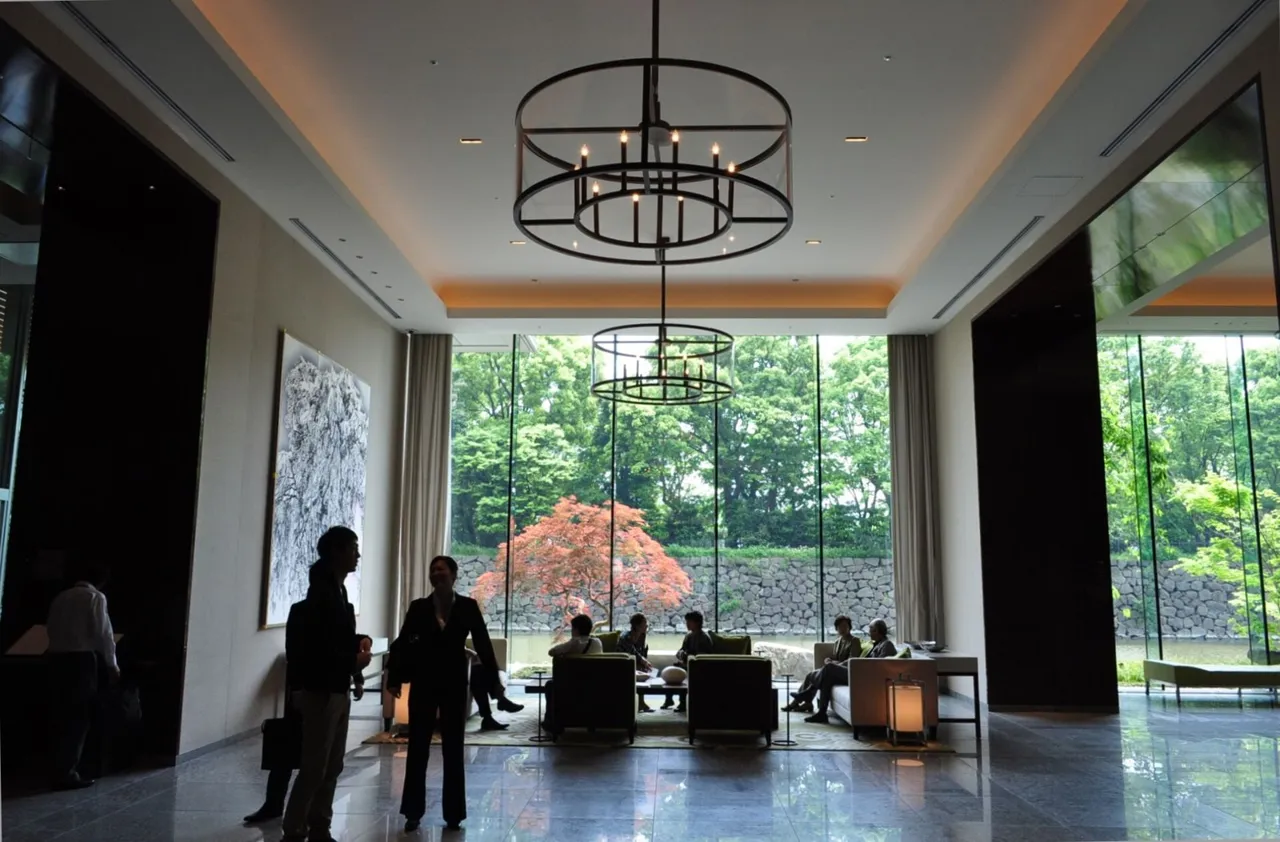 The lobby lounge of Palace Hotel Tokyo, its tall windows full of the green trees and red maple leaves of the palace moat, with figures in silhouette