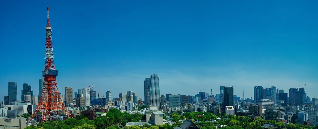 View from a Panoramic Corner King room at The Prince Park Tower Tokyo: Tokyo Tower in red and white rising above green trees, with the city skyline behind under a blue sky