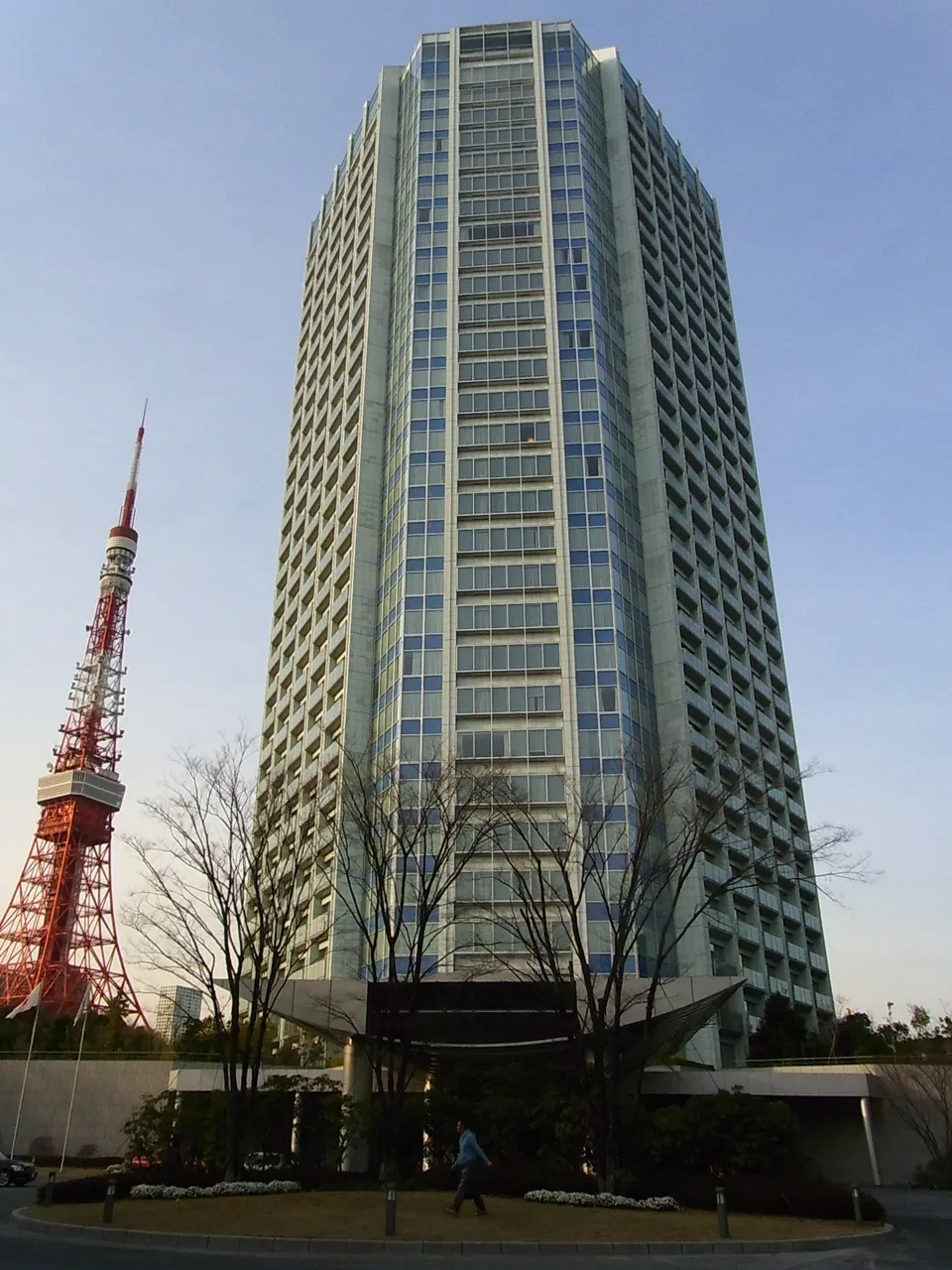 The Prince Park Tower Tokyo at dusk with Tokyo Tower standing just to its left, bare winter trees and the entrance canopy in front