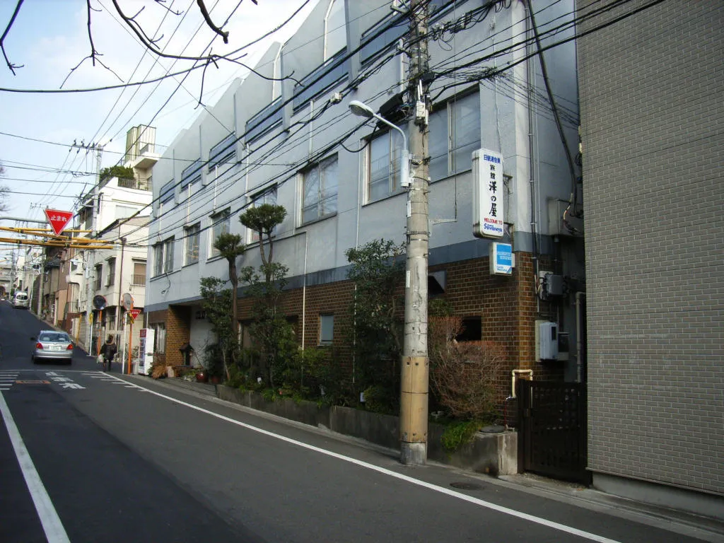 The grey three-storey front of Ryokan Sawanoya on a quiet Yanaka street, with a vertical sign bearing the inn's name and utility wires overhead