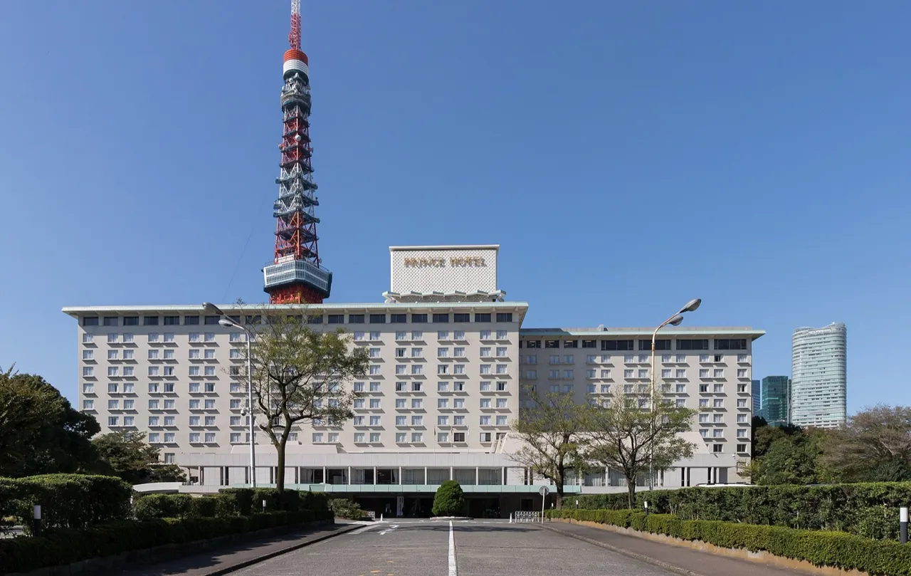 The front of the Tokyo Prince Hotel with its rooftop sign, and Tokyo Tower rising directly behind it against a blue sky