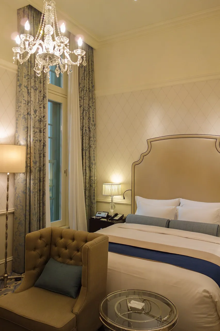 A Dome Side guest room at the Tokyo Station Hotel: a high ceiling with a chandelier, cream walls and a bed with a padded headboard