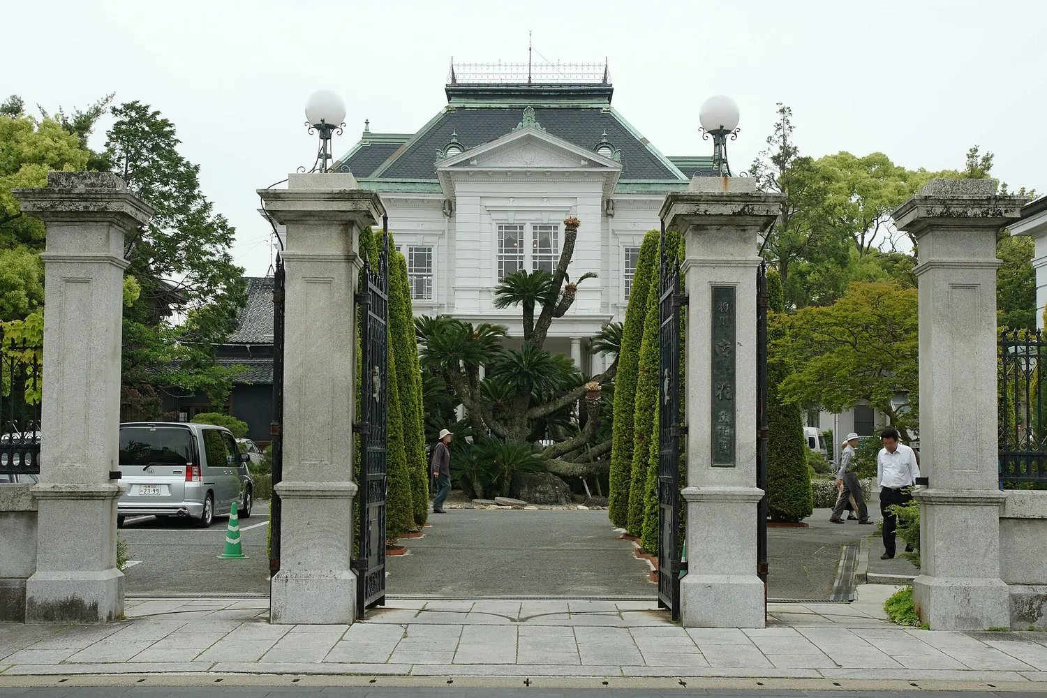 Stone gateposts in front of a white Western-style house with a green roof