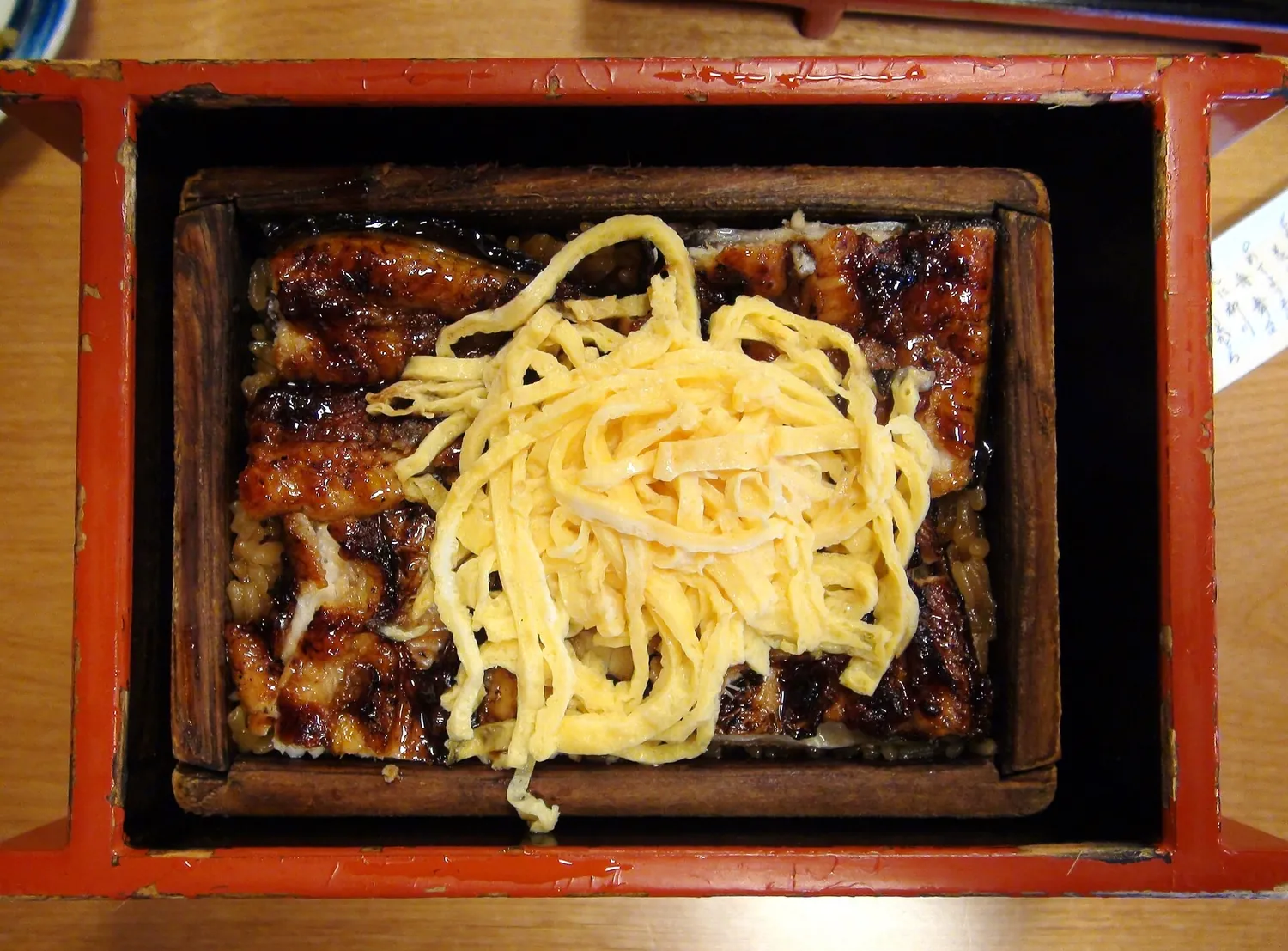 Grilled eel on rice in a red lacquered box, topped with a heap of thin yellow egg strips
