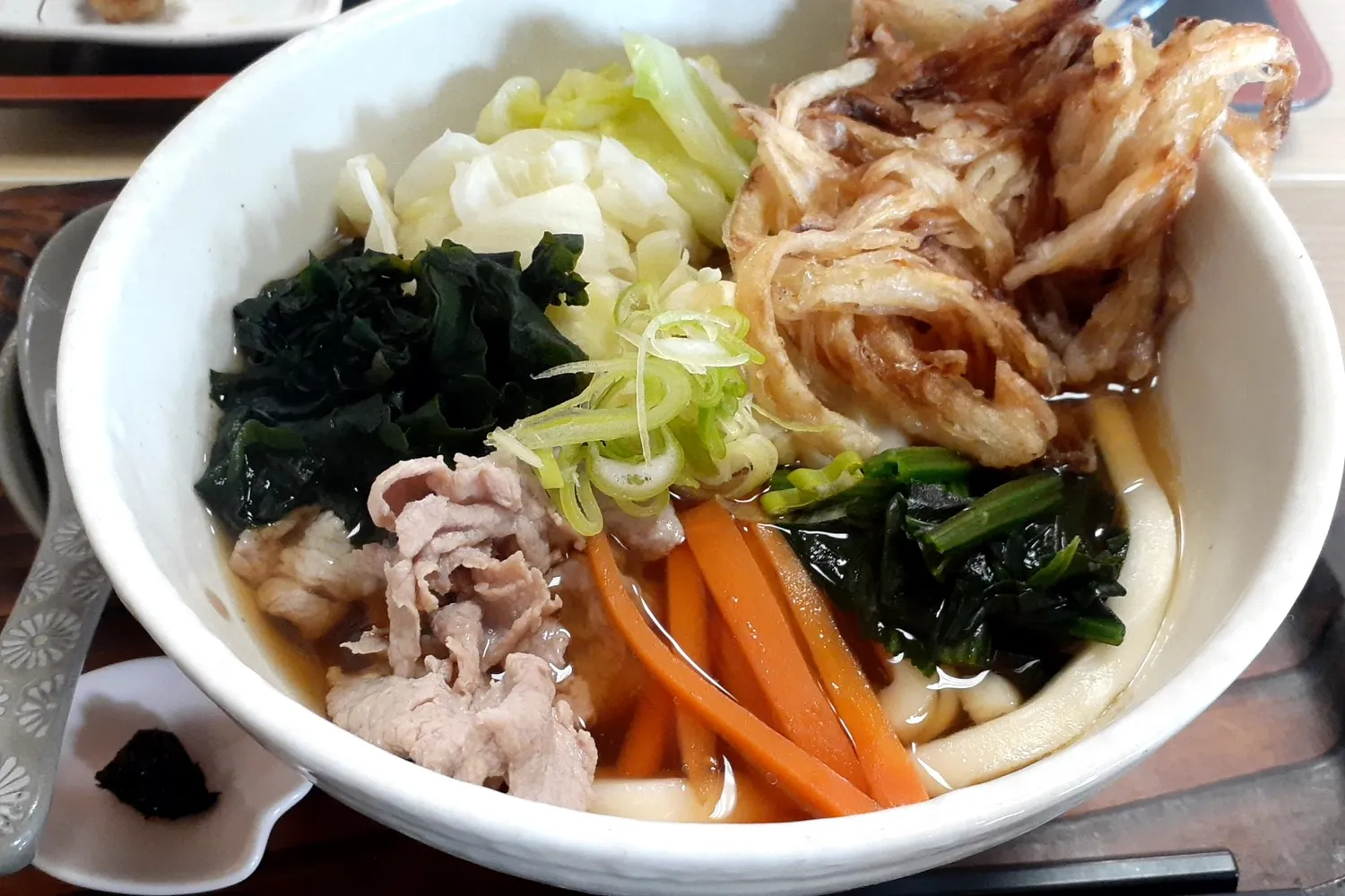 A bowl of udon piled with pork, carrot, wakame, cabbage and a large vegetable tempura