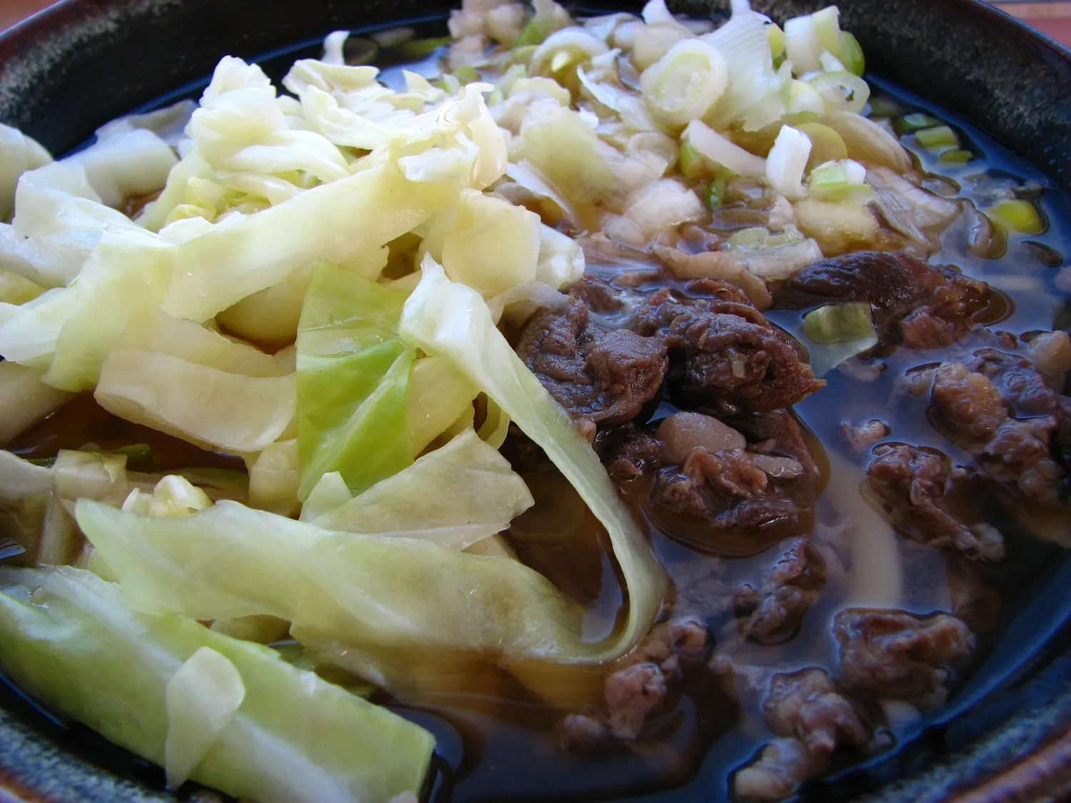Thick udon in dark broth under a heap of boiled cabbage and simmered horse meat