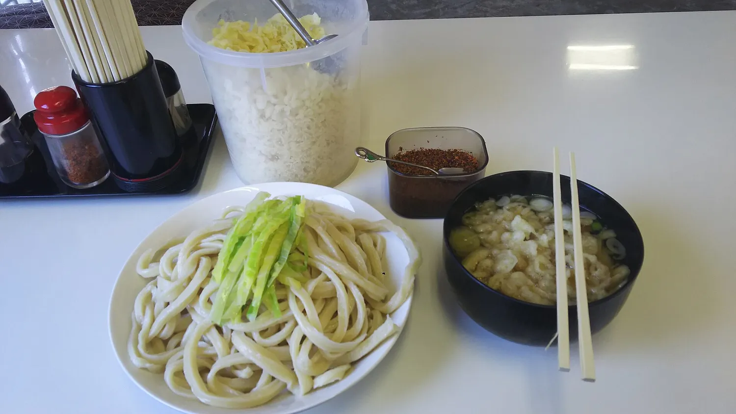 A plate of thick udon with green onion beside a bowl of broth, with a small dish of reddish-brown suridane paste